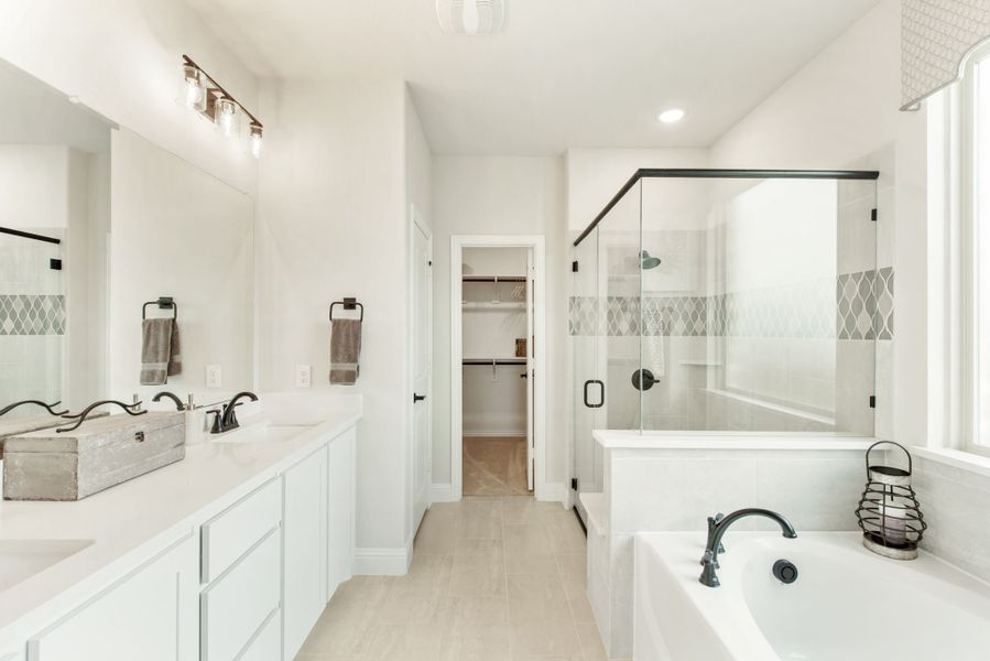 Master bathroom with double vanity, glass walk-in shower, soaking tub, and walk-in closet access