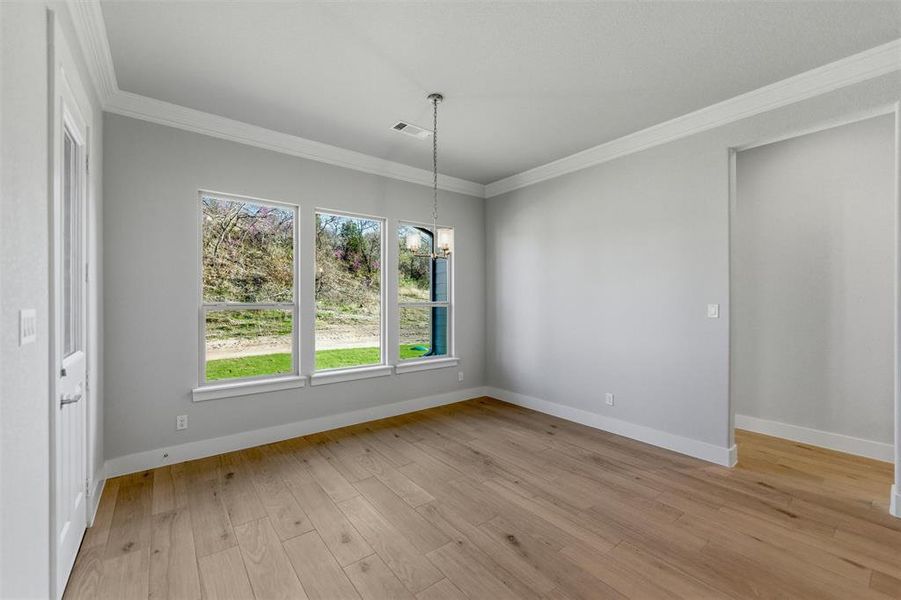 Unfurnished dining area featuring ornamental molding, light wood-style flooring, and hanging lights