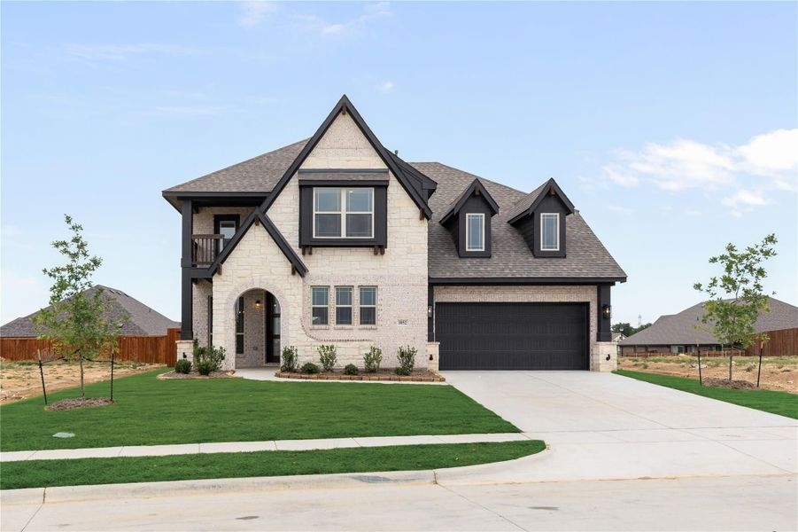 Two-story home with light stone exterior, dark trim, arched entry, and two-car garage with green front lawn Two-story home with light stone exterior, dark trim, arched entry, and two-car garage with green front lawn