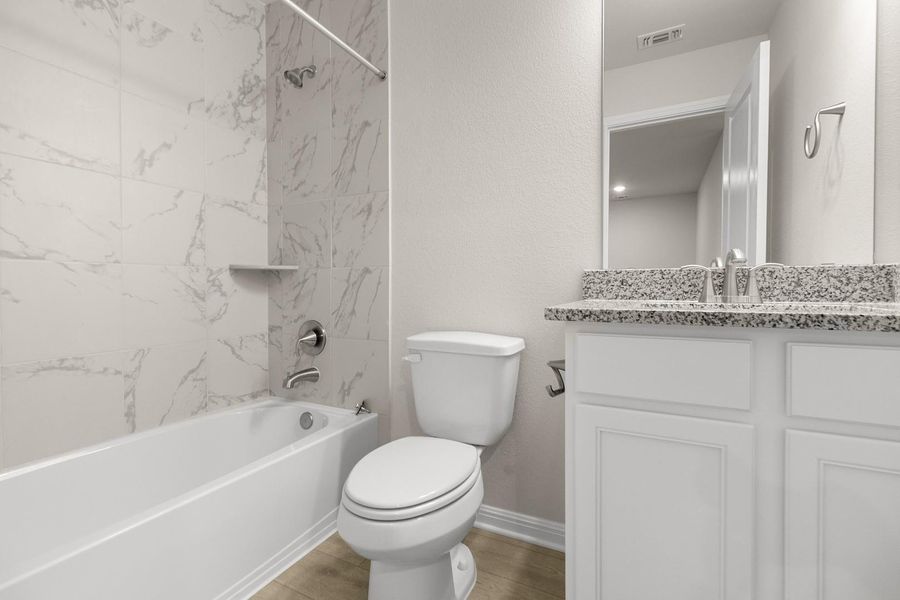 Bathroom featuring a white bathtub with a tile surround, a toilet, and a vanity with a granite countertop and white cabinetry
