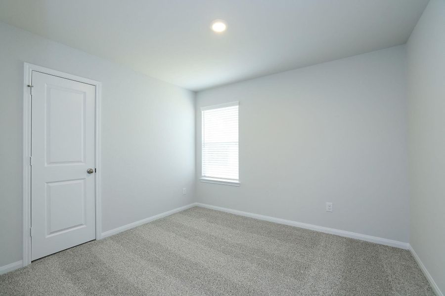Bedroom #2 offers a single window dressed with blinds, and neutral carpet flooring. It features a simple white door and overhead lighting, ideal for a bedroom or office space.