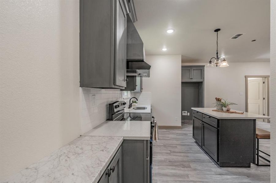 Kitchen featuring stainless steel electric range oven, a breakfast bar, backsplash, a center island, and gray cabinets