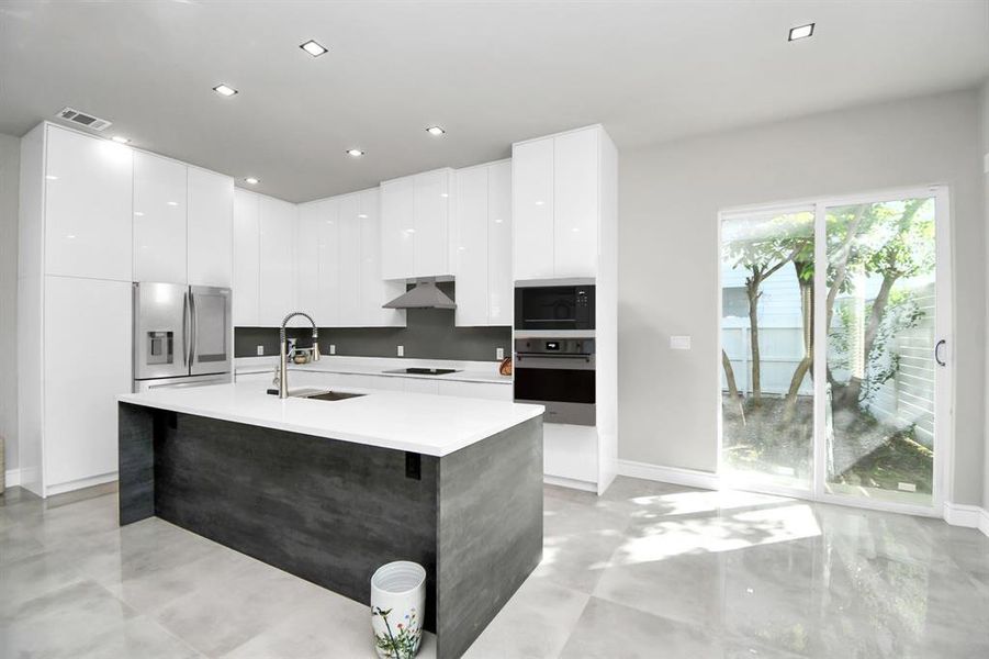 You're looking at a modern kitchen with sleek white cabinetry, a large island with a dark finish, and built-in appliances. The room features ample natural light and a minimalist design.(appliances in this photo is virtually staged, appliances will be installed)