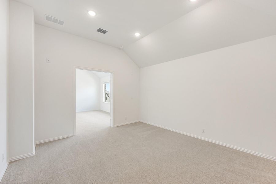 Empty room with vaulted ceiling, recessed lighting, and beige carpet with doorway to adjoining room Empty room with vaulted ceiling, recessed lighting, and beige carpet with doorway to adjoining room