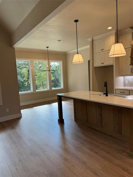 Kitchen with decorative light fixtures, light wood finished floors, light stone counters, a textured ceiling, and crown molding Kitchen with decorative light fixtures, light wood finished floors, light stone counters, a textured ceiling, and crown molding
