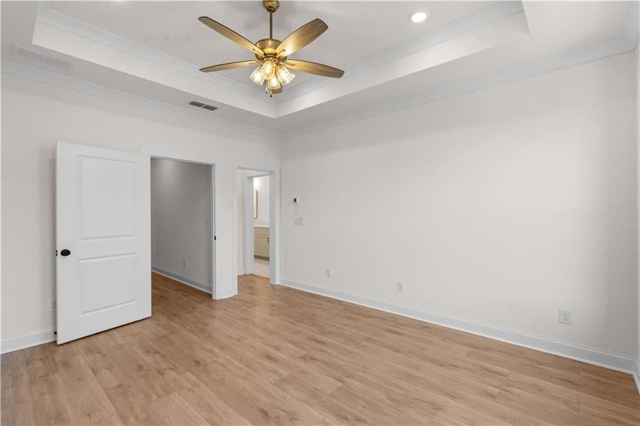 Unfurnished bedroom featuring a raised ceiling, crown molding, light wood-style floors, ceiling fan, and recessed lighting