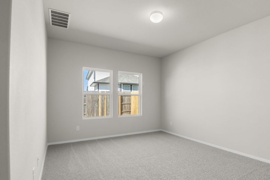 Image of a primary bedroom with cream walls, tan carpeting. two windows and white trim