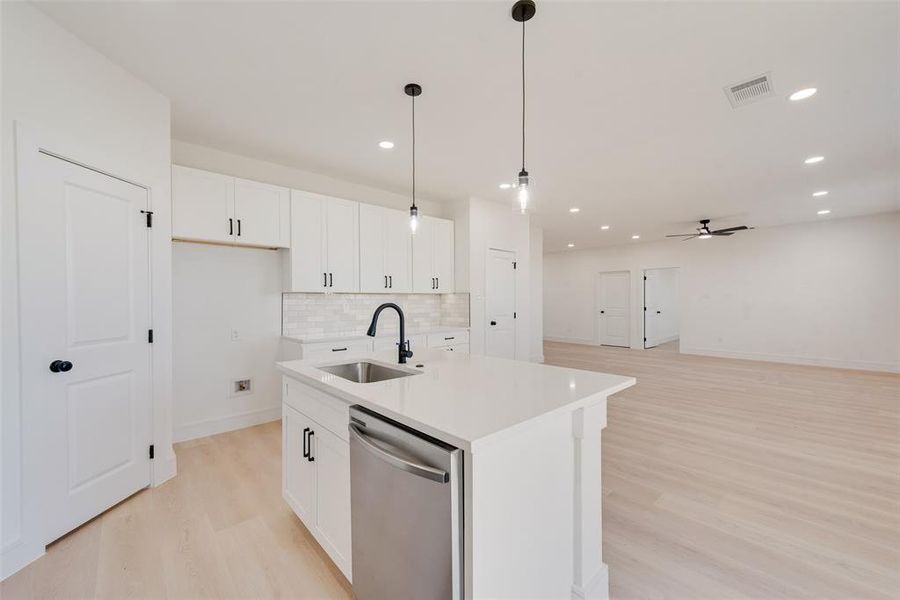 Kitchen featuring ceiling fan, sink, stainless steel dishwasher, pendant lighting, and a center island with sink