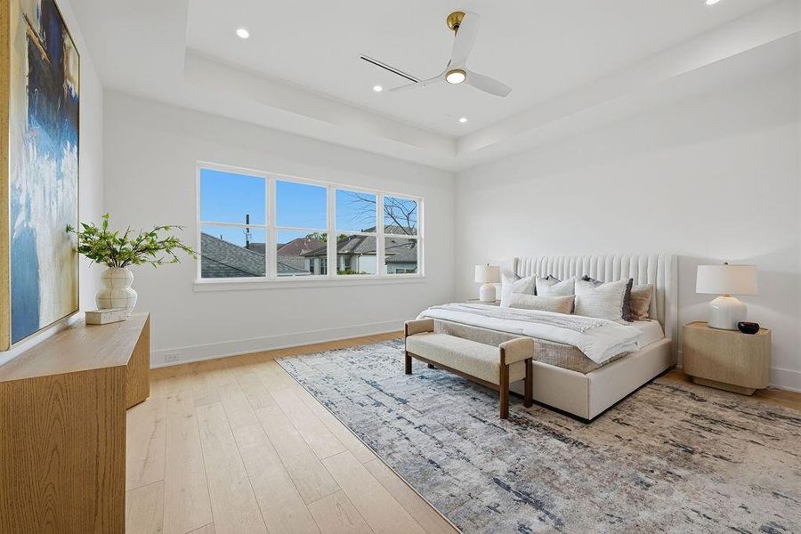 A Serene Sanctuary of Scale and Design. The expansive primary suite serves as a tranquil retreat, balancing architectural volume with soft, organic textures. Defined by a dramatic deep tray ceiling and wide-plank oak flooring, the room offers a spacious layout that comfortably accommodates a king-sized suite and a dedicated lounge or vanity area