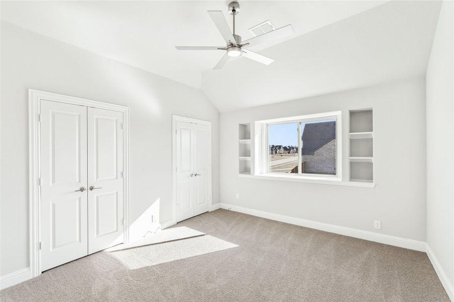 Empty bedroom with vaulted ceiling, ceiling fan, double closet, and built-in shelves beside window Empty bedroom with vaulted ceiling, ceiling fan, double closet, and built-in shelves beside window