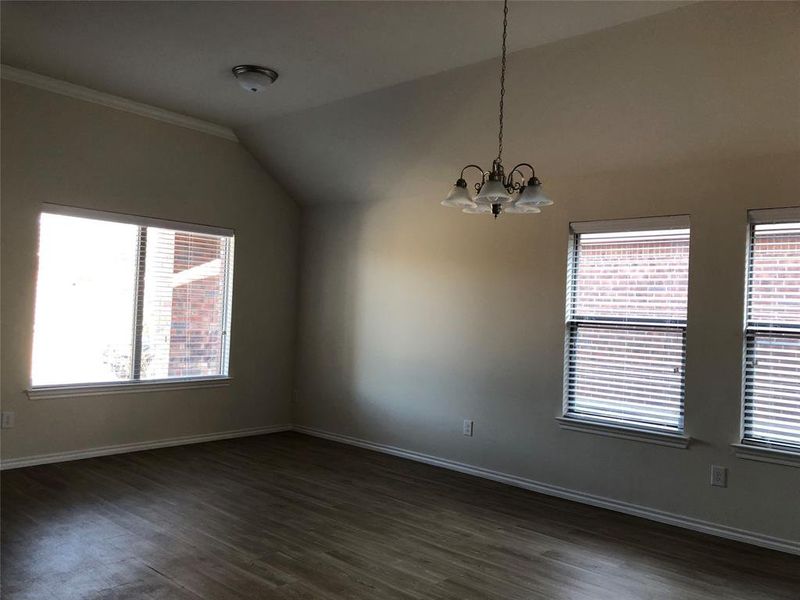 Empty room featuring dark hardwood / wood-style flooring, lofted ceiling, and an inviting chandelier