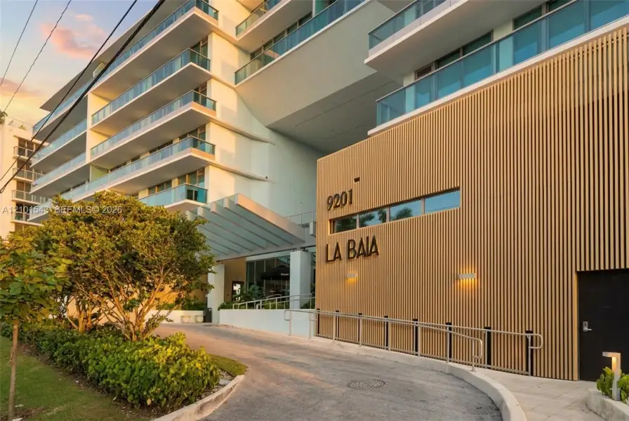 Contemporary architectural exterior featuring vertical wood-slat cladding, multi-level balconies with glass railings, and a covered porte-cochère entry