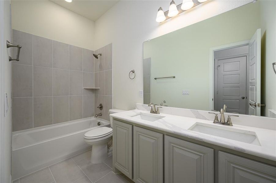 Full bathroom with tiled shower / bath, tile patterned flooring, double vanity, and toilet