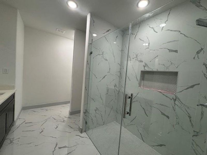 This is a modern bathroom featuring a spacious walk-in shower with glass doors and stylish marble-look tiles. A vanity area is visible to the left.