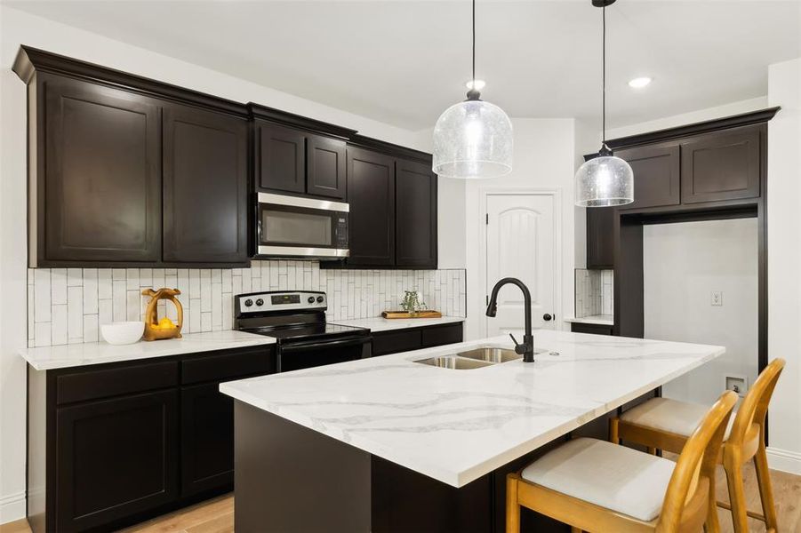 Kitchen featuring range with electric cooktop, a center island with sink, decorative backsplash, sink, and decorative light fixtures