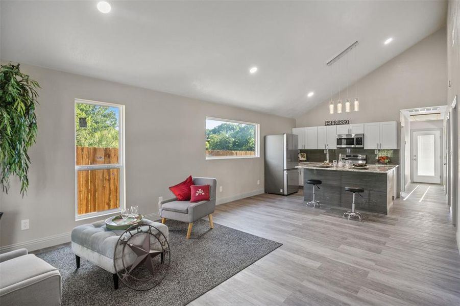 Living room featuring healthy amount of natural light, recessed lighting, light wood-style flooring, and high vaulted ceiling