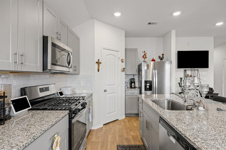 Kitchen featuring stainless steel appliances, gray cabinetry, light wood-type flooring, decorative backsplash, and light stone counters