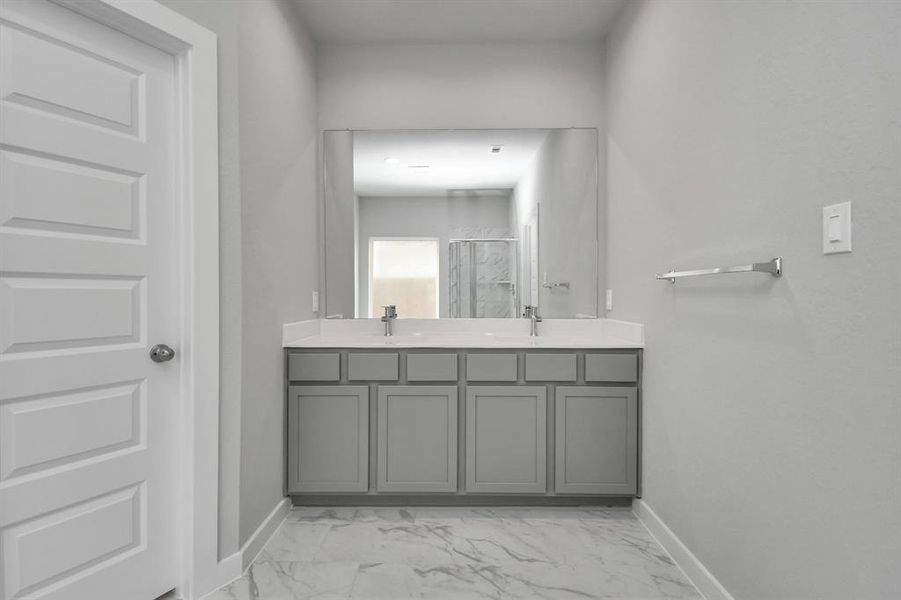 The sophisticated vanity, featuring double sinks, light-colored countertops, contemporary hardware, and bright recessed lighting, adds both style and functionality to the space.