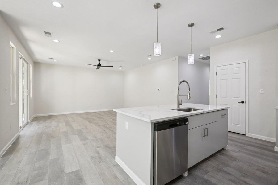 Kitchen featuring dishwasher,  light wood-type laminate flooring, an island with sink, a ceiling fan, and decorative light fixtures