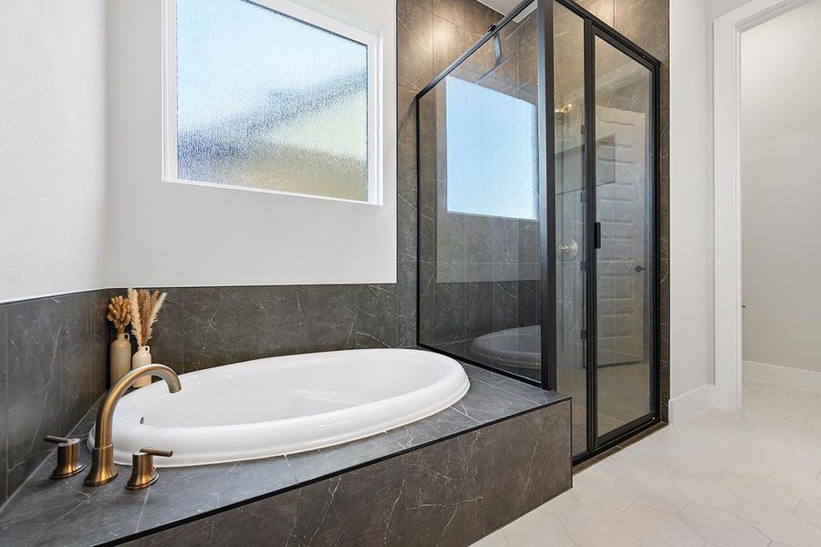 Dark stone tile surrounds a deep soaking tub and a modern glass shower.