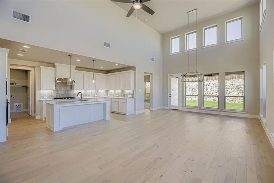 Kitchen featuring open floor plan, white cabinetry, a kitchen island with sink, backsplash, and light wood-type flooring