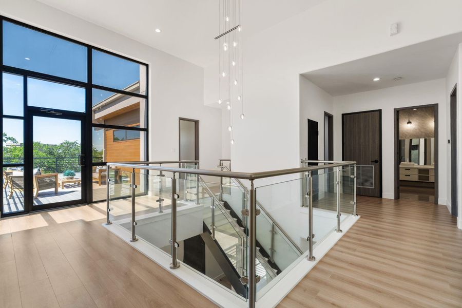 The second-floor landing is a transition space with its own presence — a chrome and glass stair railing, a multi-drop pendant light fixture, and a floor-to-ceiling black-framed window that frames a view toward the open air deck.