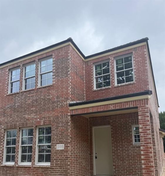 Brick exterior featuring a covered entry, white-framed windows, dark roofline, and light-colored trim accents Brick exterior featuring a covered entry, white-framed windows, dark roofline, and light-colored trim accents
