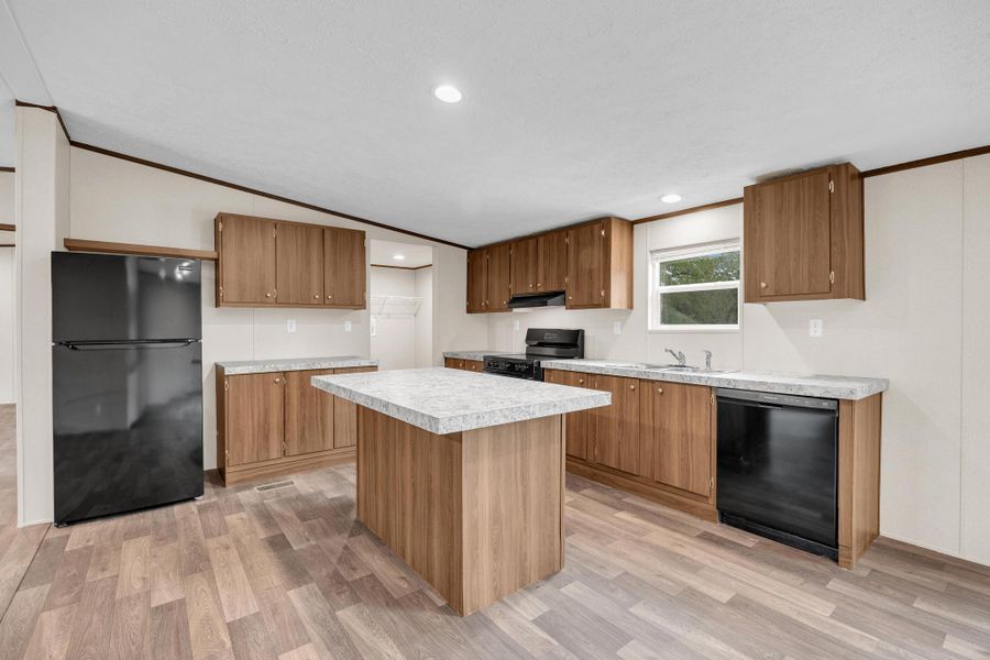Kitchen with black appliances, ornamental molding, light wood finished floors, light countertops, and a kitchen island