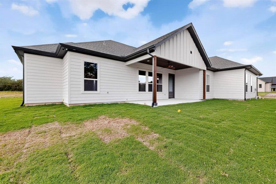 Back of property with roof with shingles, a patio, board and batten siding, and a yard