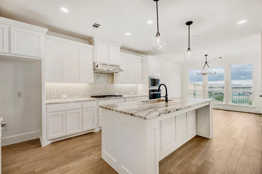 Bright kitchen featuring a large central island with a stone-finish countertop, white cabinetry, and wood-finish flooring