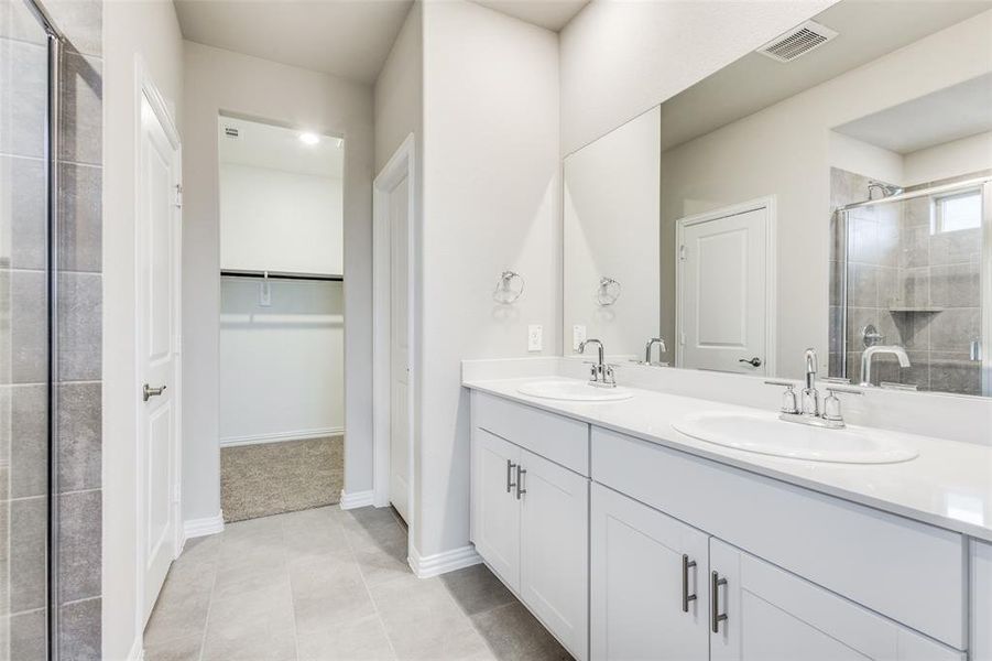Full bathroom featuring a shower stall, double vanity, a walk in closet, and light tile patterned floors