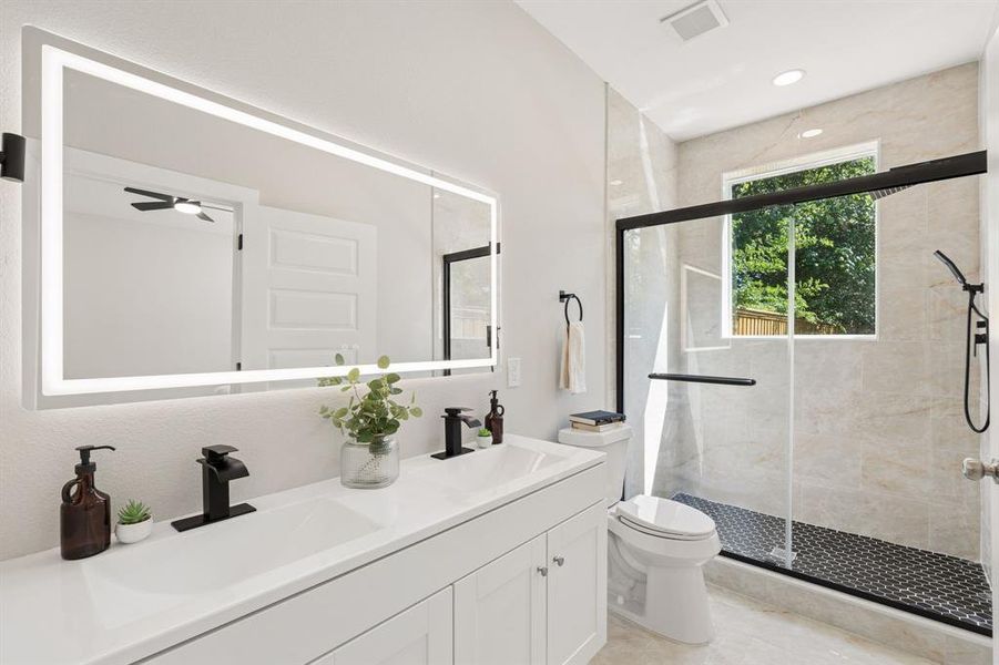 Dual vanity with integrated sinks and black matte fixtures, illuminated by a large back-lit mirror Dual vanity with integrated sinks and black matte fixtures, illuminated by a large back-lit mirror