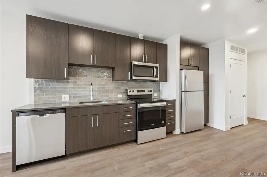 Contemporary kitchen with quartz countertops, stainless steel appliances, tile backsplash, and ample cabinet storage.