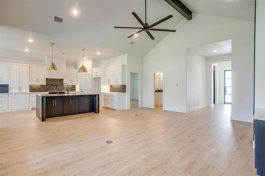 Kitchen featuring an island with sink, beam ceiling, light wood-type flooring, hanging light fixtures, and white cabinets