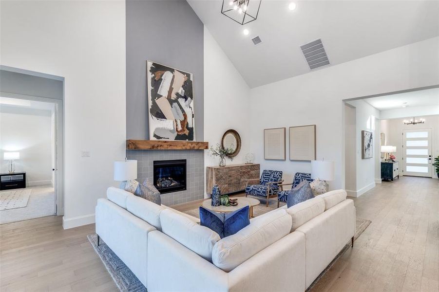 Living area with a chandelier, high vaulted ceiling, light wood-style flooring, and a glass covered fireplace Living area with a chandelier, high vaulted ceiling, light wood-style flooring, and a glass covered fireplace