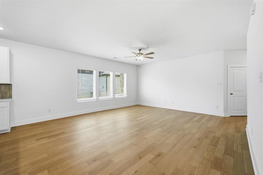 Spacious room featuring wood-finish flooring, white walls, and a ceiling fan