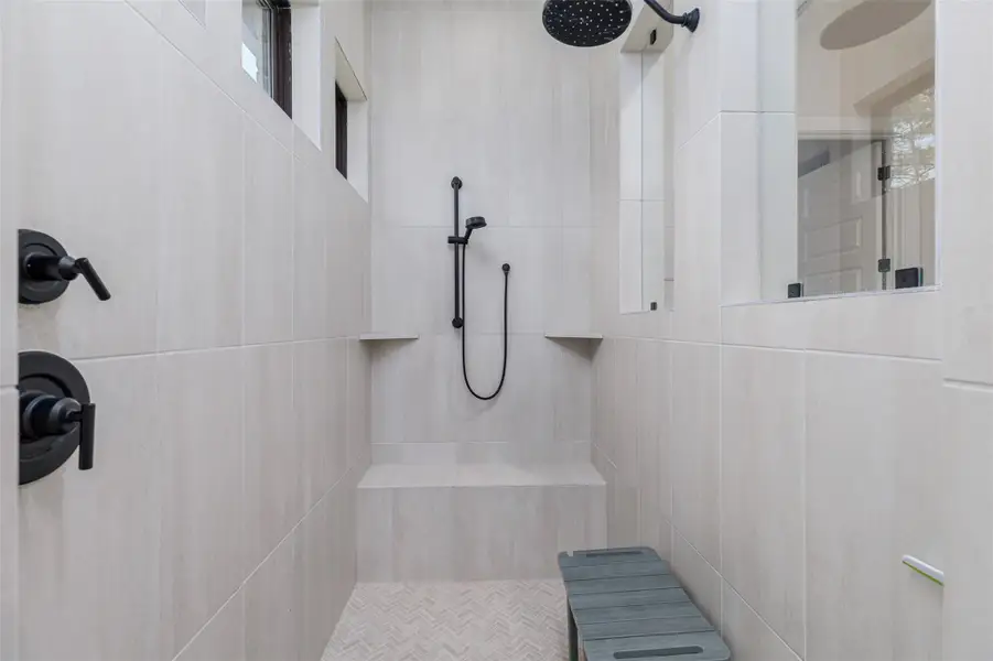 Built in shelves and a seating area.  How thoughtful to place the faucet controls to the immediate left side on entry and a glass door to keep the heat in.  A pretty herring bone tile floor further compliments this very contemporary and luxurious shower room.