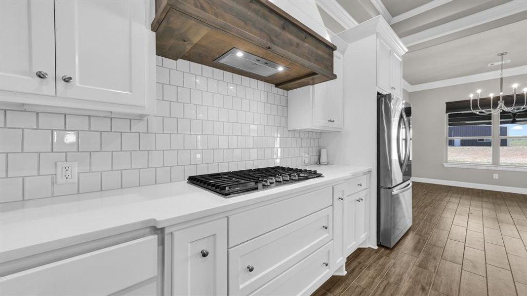 Kitchen with premium range hood, backsplash, stainless steel appliances, ornamental molding, and white cabinetry