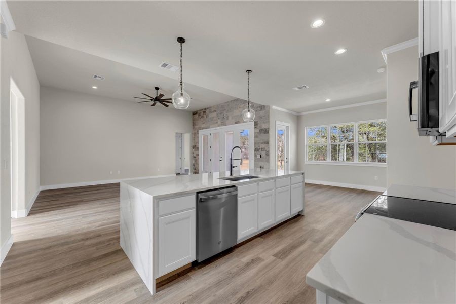 Kitchen with white cabinets, a center island with sink, light stone countertops, open floor plan, and crown molding