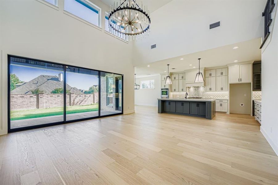 Unfurnished living room with light wood finished floors, a towering ceiling, a chandelier, and recessed lighting Unfurnished living room with light wood finished floors, a towering ceiling, a chandelier, and recessed lighting