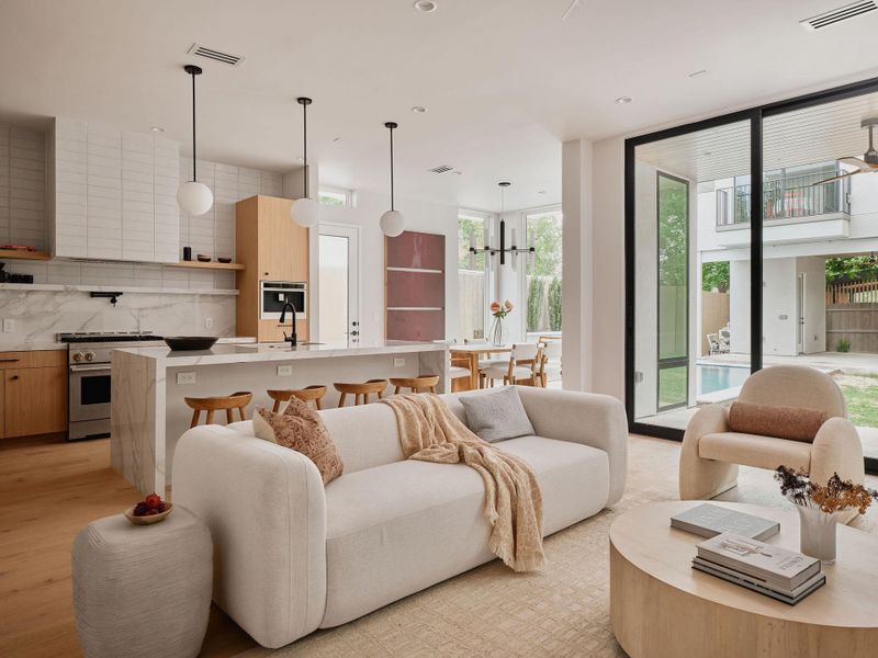 Open-concept living space featuring wood-finish flooring, a kitchen island with seating, a gas range, a white tile backsplash, and full-height glass doors opening to a backyard with a pool