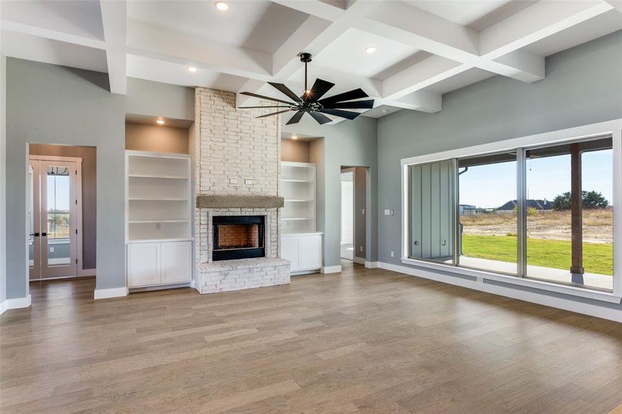 Unfurnished living room with a fireplace, light wood finished floors, coffered ceiling, beam ceiling, and ceiling fan Unfurnished living room with a fireplace, light wood finished floors, coffered ceiling, beam ceiling, and ceiling fan