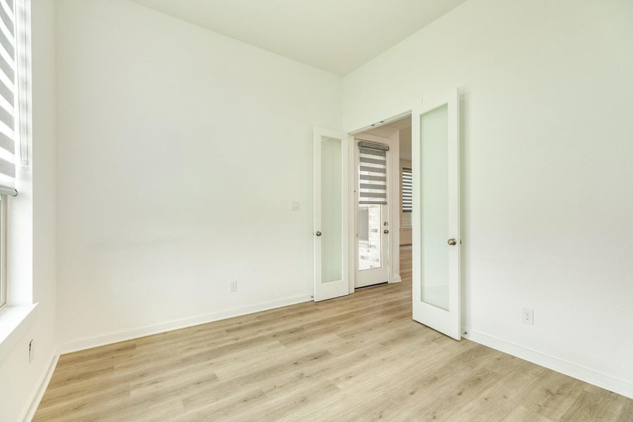 Spacious home office located just off the living area, featuring elegant double glass doors and a large window that invites abundant natural light. The room offers a peaceful view of the backyard and convenient direct sightlines to the rear door leading out to the covered patio.