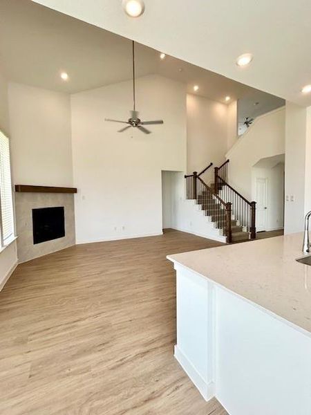 Vaulted ceiling living area featuring a fireplace with a wood mantel, wood-finish flooring, recessed lighting, and an elegant staircase with wood newel posts and black metal balusters