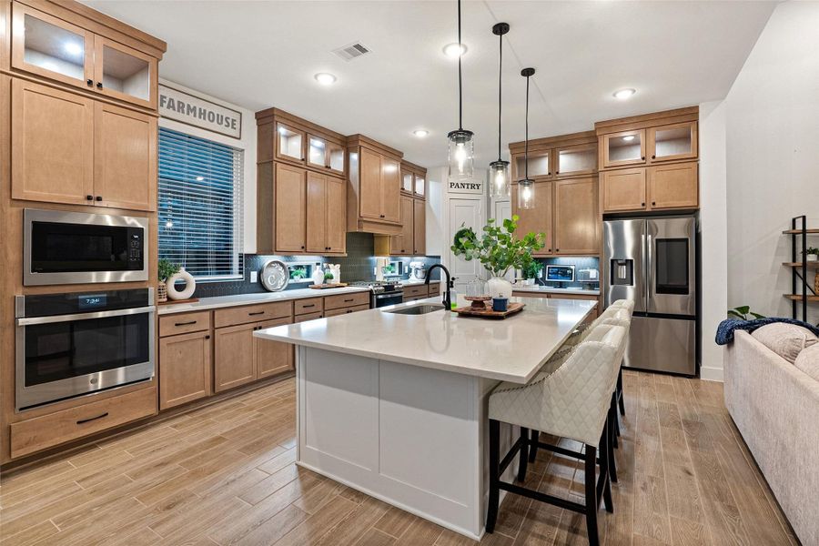 The soaring family room features high ceilings with beams, an electric fireplace wall, and flows into a chef's kitchen with quartz countertops, oversized island, luxe pantry, Barley cabinetry with glass uppers, and GE Profile appliances including double ovens with built-in air fryer. The soaring family room features high ceilings with beams, an electric fireplace wall, and flows into a chef's kitchen with quartz countertops, oversized island, luxe pantry, Barley cabinetry with glass uppers, and GE Profile appliances including double ovens with built-in air fryer.