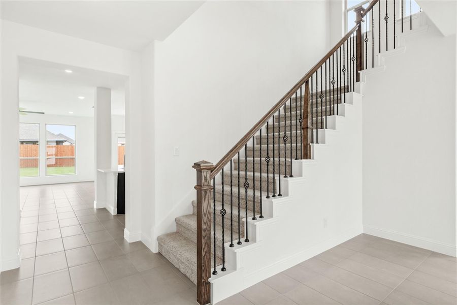Carpeted staircase with wood handrail and wrought iron balusters in a bright white entryway with tile floors Carpeted staircase with wood handrail and wrought iron balusters in a bright white entryway with tile floors