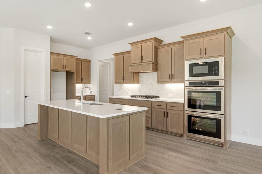 Kitchen with light wood cabinets, center island with white countertop, and stainless steel double oven and microwave