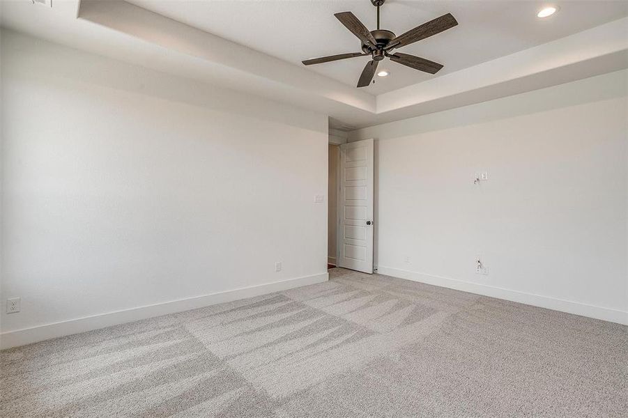 Carpeted empty room featuring a raised ceiling and ceiling fan