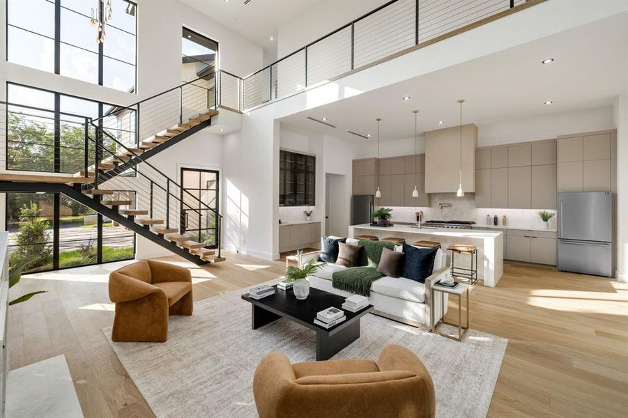 Open-concept living space featuring a two-story ceiling, light wood-finish flooring, and a contemporary floating staircase with metal railings