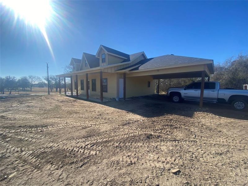 View of side of home featuring a carport, covered porch, and dirt driveway